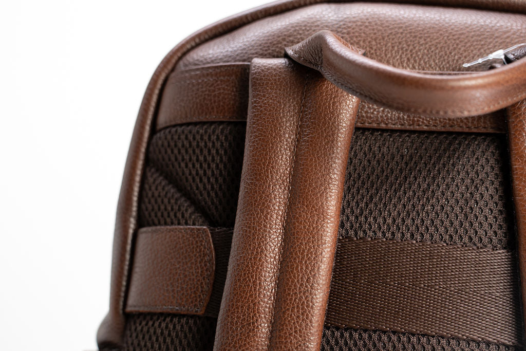 Close-up of the padded mesh back panel and leather shoulder straps on the Artelio brown backpack