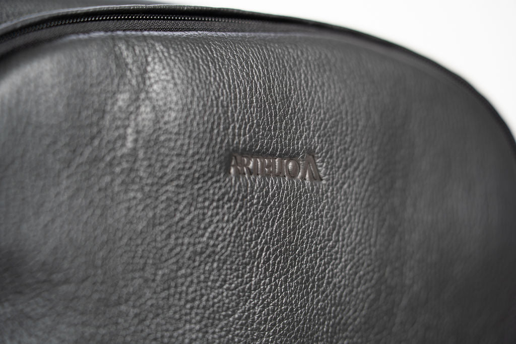Close-up of the embossed Artelio logo on the black leather backpack
