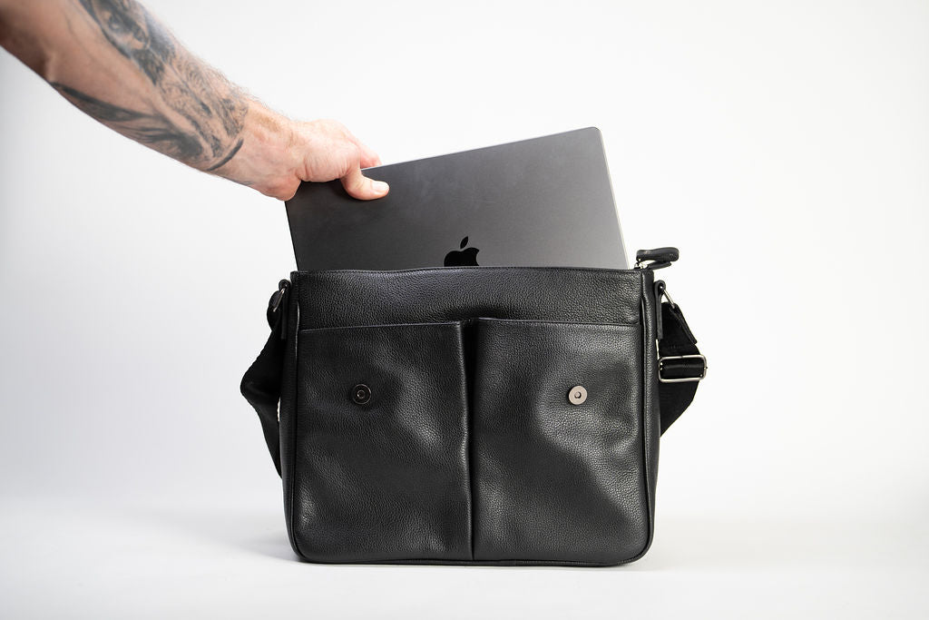 A laptop being placed inside the Artelio black leather crossbody bag to show the main compartment capacity