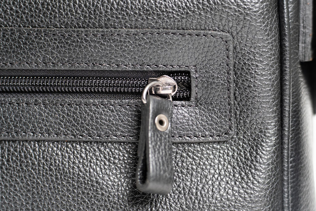 Close-up of an exterior zipper pull and stitched pocket on the Artelio black leather crossbody bag