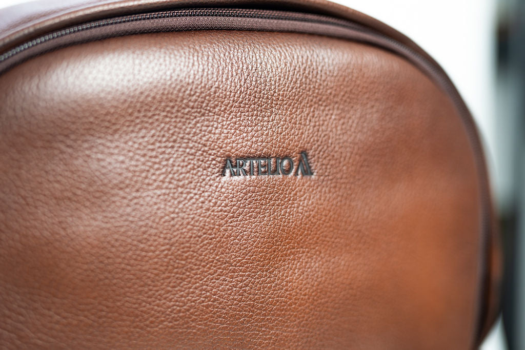 Close-up of the Artelio logo and natural grain on the brown leather backpack
