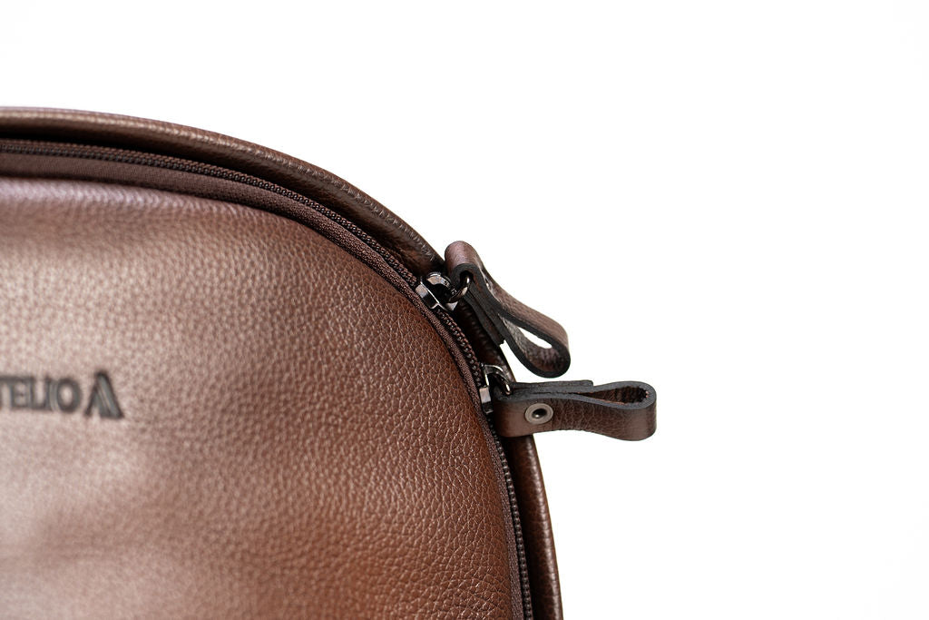 Close-up of the top zipper pulls and brown leather grain on the Artelio backpack