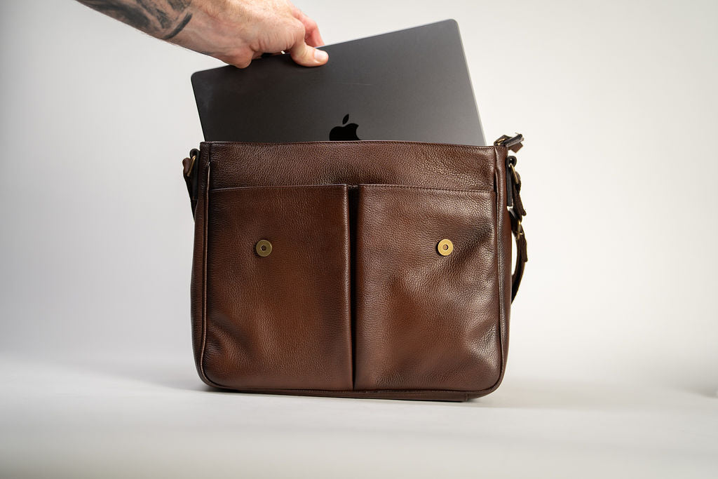 A laptop being placed inside the Artelio brown leather crossbody bag to show the main compartment capacity