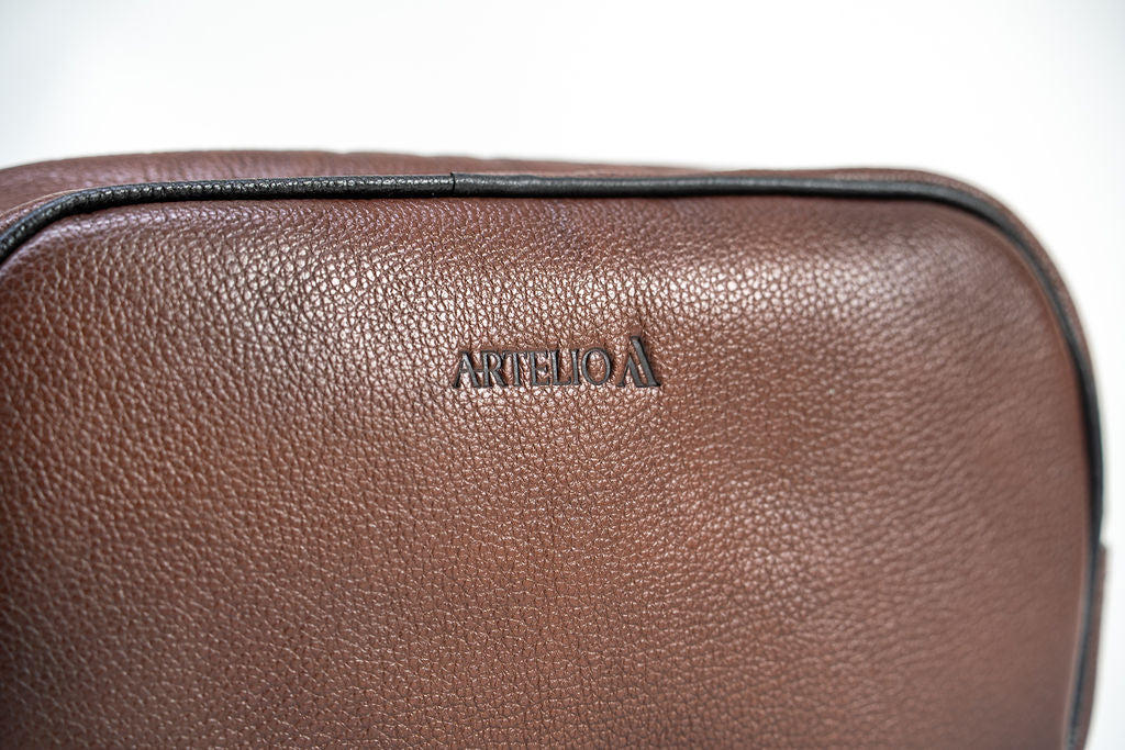 Close-up of the Artelio logo and pebbled brown leather on the dopp kit